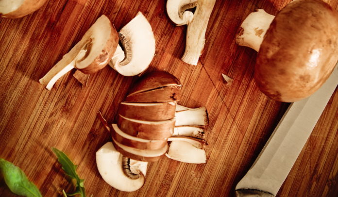 Meal preparation process. Knife, salad, mushrooms on the wooden background